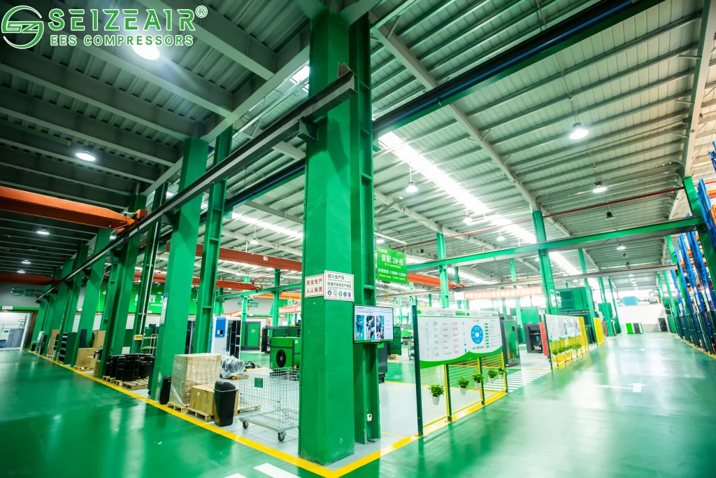 Bố trí trong xưởng gọn gàng, cột màu xanh lá cây và sơn sàn tạo ra một môi trường công nghiệp sạch sẽ, được trang bị các loại thiết bị sản xuất, khu vực lưu trữ nguyên liệu và bảng trưng bày.máy nén khí tiết kiệm điện